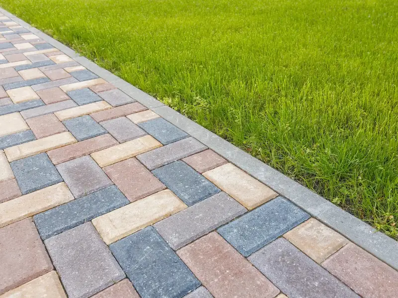 Multi-tone block paving laid to a herringbone pattern against a lawn edge